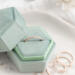  A rose gold diamond-textured stacking ring displayed inside a green velvet hexagonal ring box, with additional rings scattered beside it.